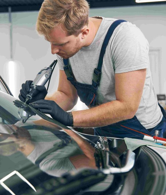 Car service technician checks crack on car windshield closeup. Auto glass repair. Man in workshop